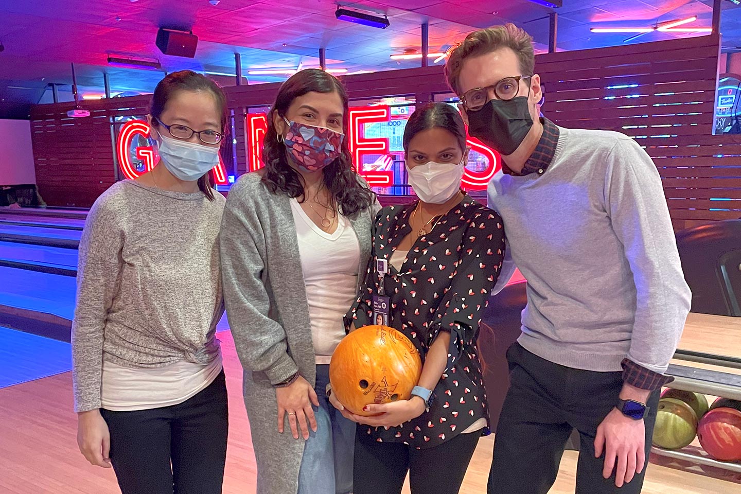 Four fellows wearing face masks and posing with a bowling ball in bowling alley
