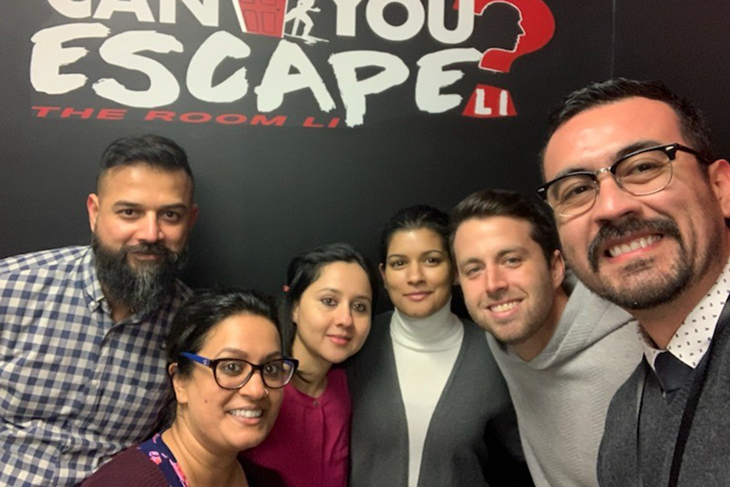 A group of fellows and Dr. Sukhminder K. Sahansra pose in front of an escape room sign that says Can You Escape?