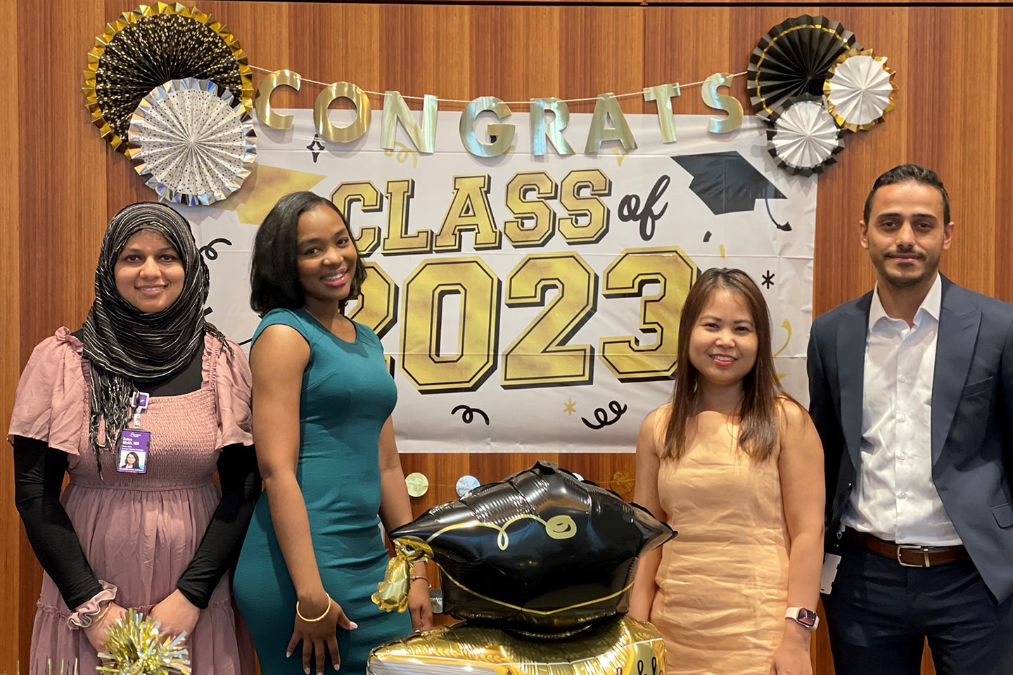 Four fellows pose in front of balloons and banners that read Congrats Class of 2023