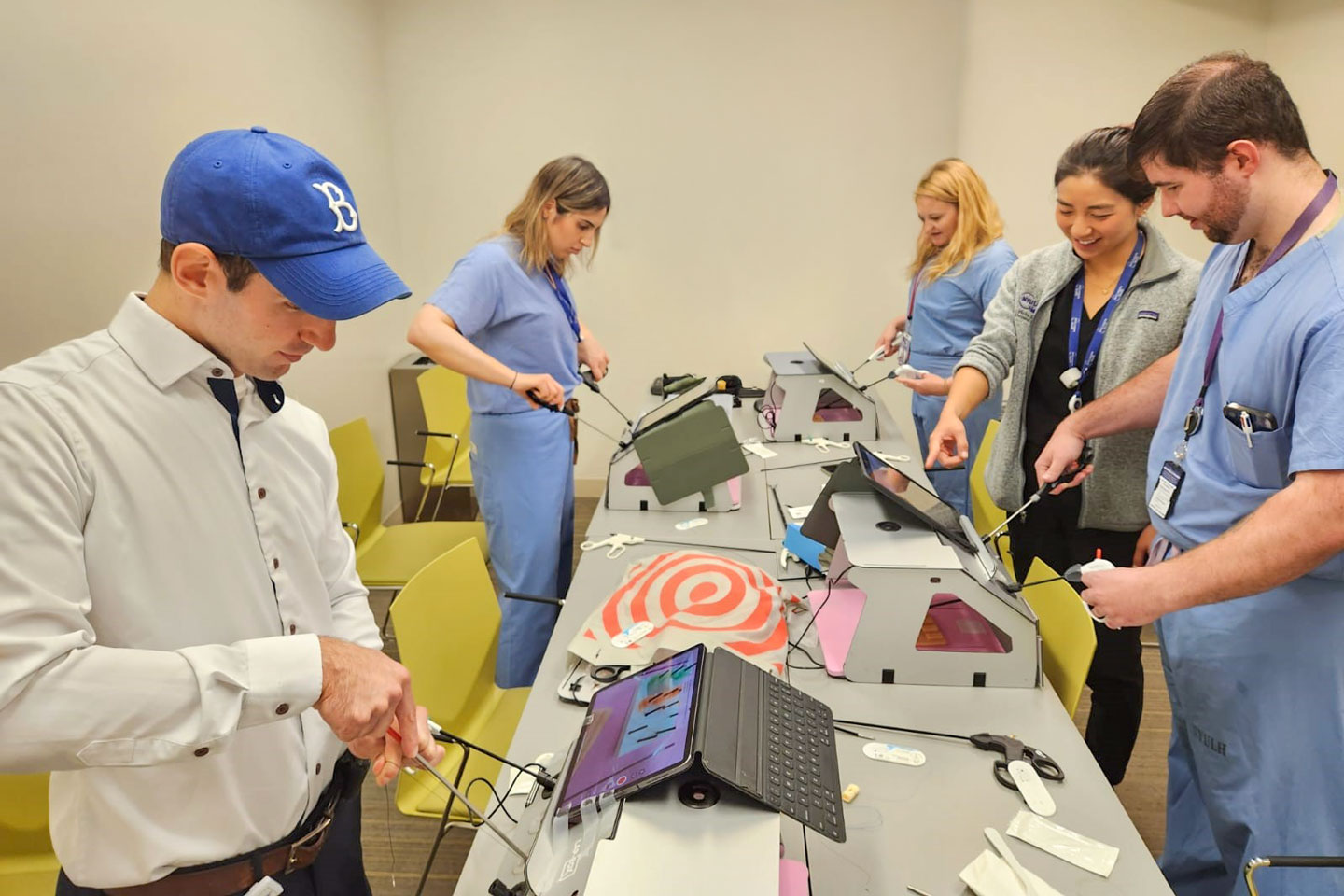 Students engage in a medical simulation exercise using laparoscopic training kits in a classroom setting. 